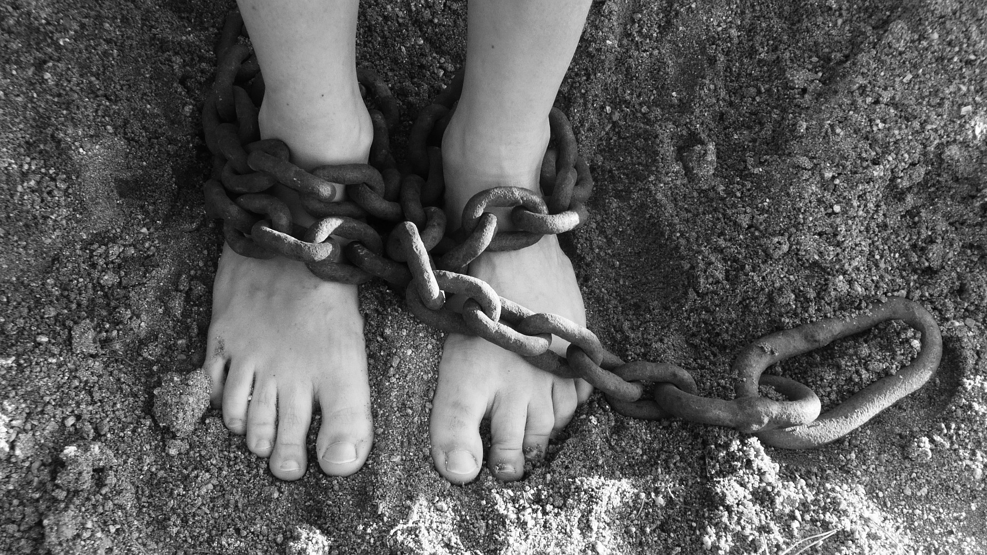 Feet in sand with chains around ankles